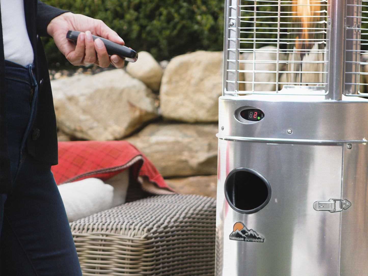 Close up of the Illume Patio Heater in Stainless Steel. Model is close to heater with remote control.