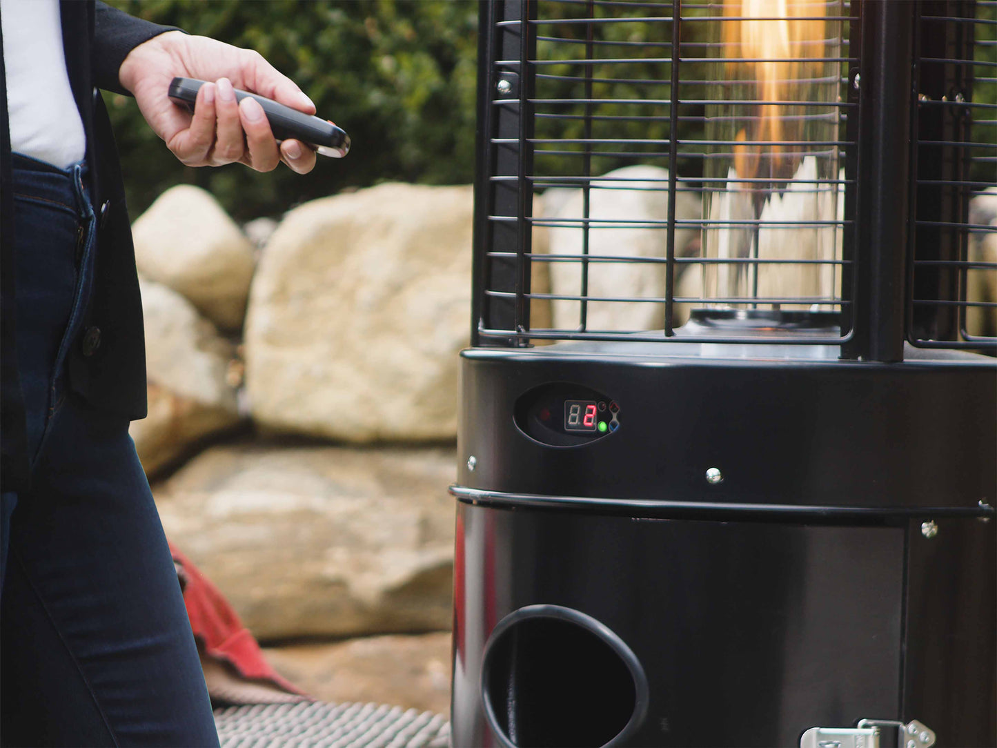 Close up of Illume Patio Heater in Black with digital control panel. Model is nearby with remote control.