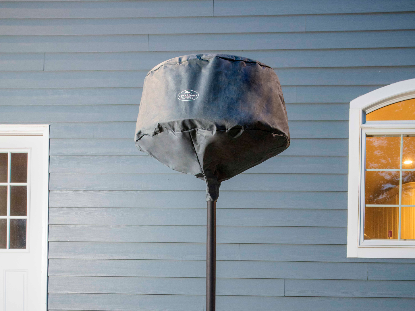 Close up of Glow Freestanding Patio Heater with Cover. Blue siding and house windows are behind the heater.